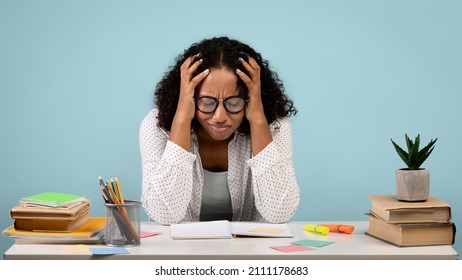 Tired African American female student crying over books and notebooks, studying for difficult exam on blue studio background, banner. Exhausted black woman preparing for college test