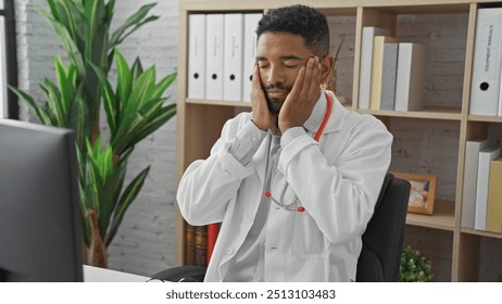 A tired african american male doctor in a clinic office, expressing stress or headache while indoors. - Powered by Shutterstock