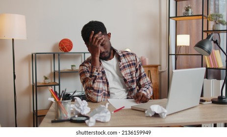 Tired African American man freelancer teacher use laptop computer, suffering from tension migaine headache after e-learning remote working job with pupils sitting at home office table. Guy businessman