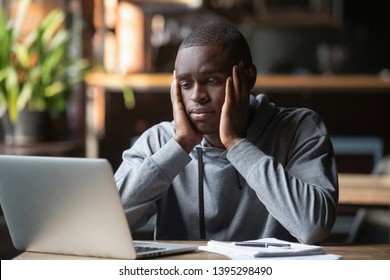 Tired African American Man Working On Laptop In Coffeehouse, Holding Head In Hands, Looking At Screen, Exhausted Student Taking Break, Watching Webinar, Working On Research Work Or Homework In Cafe