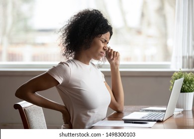 Tired African American Millennial Female Worker Sit At Desk Touch Back Suffer From Lower Spinal Spasm, Hurt Unhealthy Biracial Woman Stretch Have Strong Backache, Incorrect Posture Concept