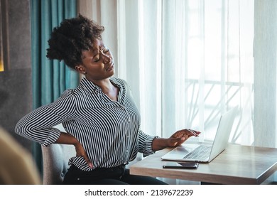 Tired African American Millennial Female Worker Sit At Desk Touch Back Suffer From Lower Spinal Spasm, Hurt Unhealthy Biracial Woman Stretch Have Strong Backache, Incorrect Posture Concept