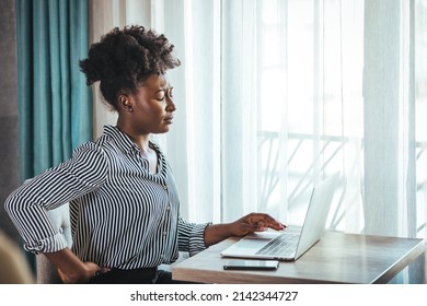 Tired African American Millennial Female Worker Sit At Desk Touch Back Suffer From Lower Spinal Spasm, Hurt Unhealthy Biracial Woman Stretch Have Strong Backache, Incorrect Posture Concept