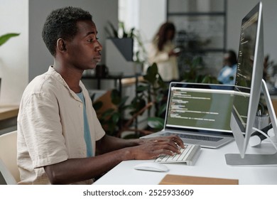 Tired African American programmer coding in cozy office full of plants and electronic devices