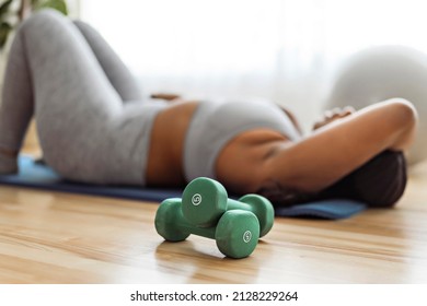 A Tired African American Woman Working Out In Home Livingroom Gym With Dumbbell In Font View Focus