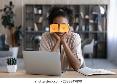 Tired Afro American millennial student girl sleeping at workplace with paper notes, drawn eyes on eyeglasses. Sleepy lazy remote employee sitting at laptop, feeling fatigue, overworked, energy reduce - Powered by Shutterstock