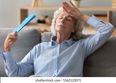 Tired Annoyed Senior Woman Holding Waving Fan Feel Hot Sit On Sofa At Home Without Air Conditioner, Overheated Exhausted Old Elder Grandma Sweating Suffer From Hormone Problem Summer Heat Concept