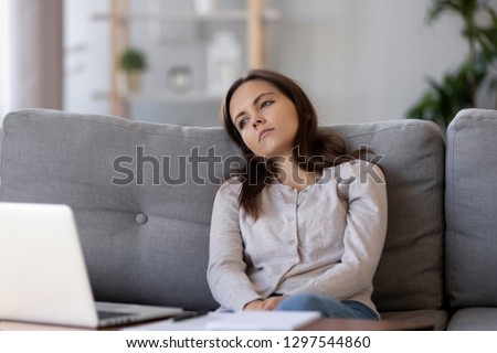 Tired apathetic teenager looking away sitting on couch disinterested in study work, unhappy depressed thoughtful young woman bored alone at home feeling demotivated melancholic lost in thoughts