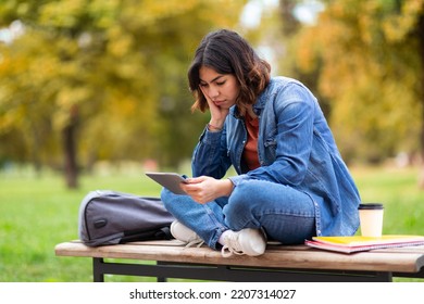 Tired Arab Student Woman Using Digital Tablet While Sitting On Bench Outdoors, Bored Young Middle Eastern Female Spending Time With Modern Gadget While Resting Outside In Autumn Park, Copy Space