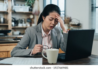 tired asian businesswoman feeling dizzy from overworking is rubbing her temple. frowning korean woman looking fatigued has sore eyes so takes off glasses for a rest.