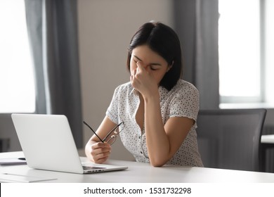 Tired Asian businesswoman taking off glasses, suffering from dry eyes syndrome after long laptop use, exhausted female employee feeling eye strain, massaging nose bridge, health problem concept - Shutterstock ID 1531732298