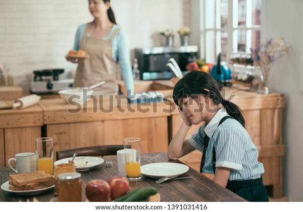 朝早く寝て朝ご飯が寝不足になるのを待つ 学校の前に服を着たアジア系の女の子が疲れた 優美な妻の母親がエプロンに忙しく手作りのおいしい健康的な食事を作る の写真素材 今すぐ編集