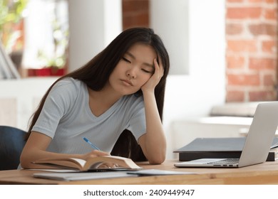 Tired Asian female student sit at desk overwhelmed with studying suffer from fatigue and exhaustion, exhausted ethnic millennial girl feel lazy unmotivated have sleep deprivation preparing for test - Powered by Shutterstock