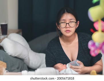 Tired Asian Mother Feeding Newborn Baby From Milk Bottle At Late Night.