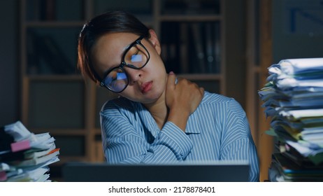 Tired Asian office employee massaging neck and shoulder muscles fatigued from using laptop computer overtime at night in office, office syndrome - Shutterstock ID 2178878401