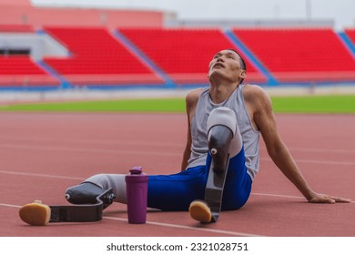 Tired Asian speed runner, equipped with two prosthetic running blades, sits on the stadium track, resting after an intense speed running practice session - Powered by Shutterstock