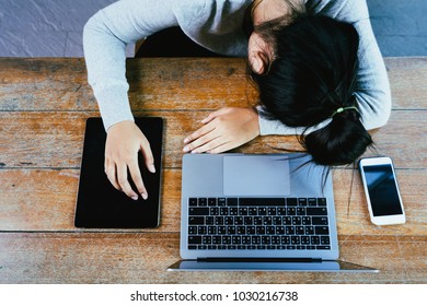 Tired Asian student sleeping on desk with laptop computer and technology device or Exhausted Businesswoman asleep on workplace