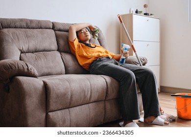 Tired Asian woman sitting on couch after cleaning the house - Shutterstock ID 2366434305