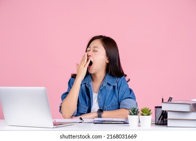 Tired Asian woman wearing casual shirt sit work at white office desk. she is yawning isolated on a pink background