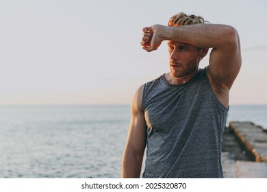 Tired athlete young strong sporty toned fit sportsman man 20s in sports clothes warm up training put hand on forehead at sunrise sun dawn over sea beach outdoor on pier seaside in summer day morning.