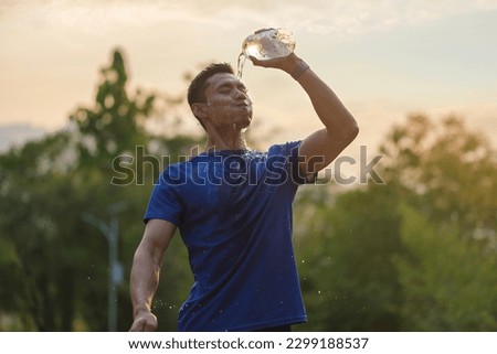 Tired athletic man cooling himself after training by squirting water into his face from a bottle.