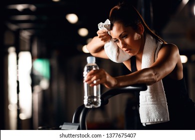 Tired Athletic Woman Wiping Sweat With A Towel While Cycling On Stationary Bicycle In A Gym. 