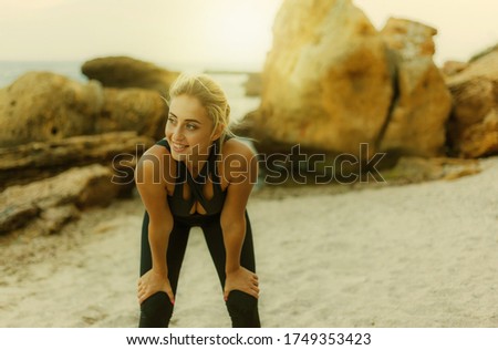 Tired attractive fitness woman in sportswear on a wild beach.