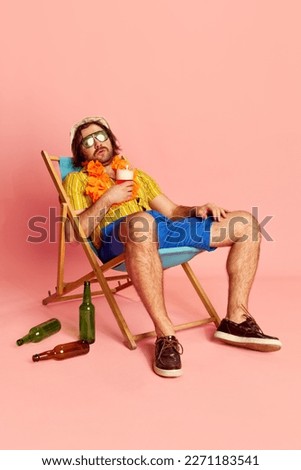 Tired beachgoer. Man in summer shirt and short with Hawaiian flower garland on chest sleeping on sun lounger over pink background. Leisure activity, vacation, summer, rest and male hobbies concept
