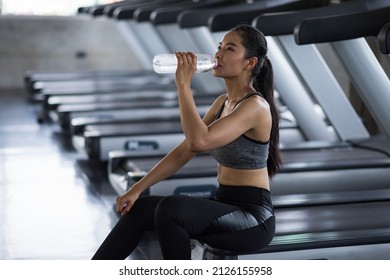 Tired Beautiful Young Asian Woman With Sweat On Body Rest And Drink Water After Break Running On Treadmills In Sport Fitness Gym. Workout, Exercise, Training For Bodybuilding And Healthy Lifestyle.