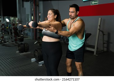 Tired Big Woman Suffering While Doing Exercises With Dumbbell Weights At The Gym With The Help Of A Male Fitness Coach 