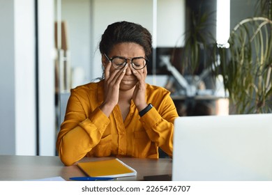 Tired black businesswoman suffering from headache and fatigue, rubbing eyes at workplace with laptop in office interior. Dry eyes, stress, deadline, pain and ill - Powered by Shutterstock