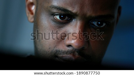 Tired black man working late at night in front of computer. Close-up face looking at screen focused and concentrated