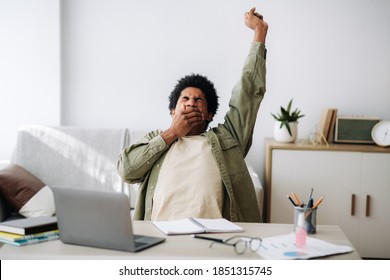 Tired black student yawning and stretching during his remote studies from home. African American youth exhausted from getting ready for test or writing coursework, feeling sleepy in front of laptop
