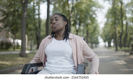 Tired black woman with disability moving in manual wheelchair, alone in park