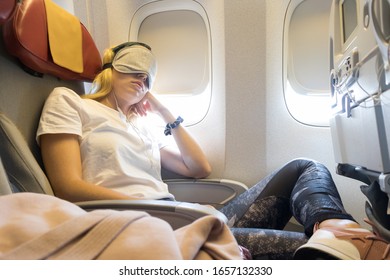 Tired Blonde Casual Caucasian Lady Napping On Uncomfortable Seat While Traveling By Airplane. Commercial Transportation By Planes.