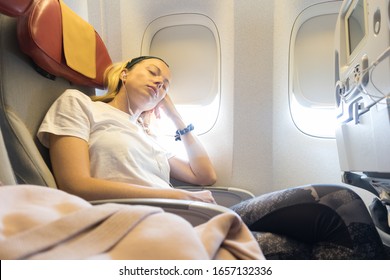 Tired Blonde Casual Caucasian Lady Napping On Uncomfortable Seat While Traveling By Airplane. Commercial Transportation By Planes.