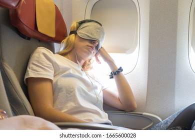 Tired Blonde Casual Caucasian Lady Napping On Uncomfortable Seat While Traveling By Airplane. Commercial Transportation By Planes.