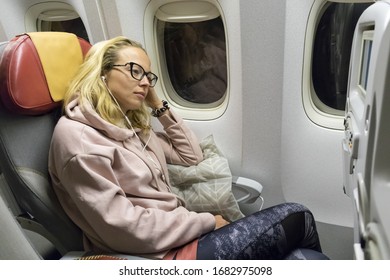 Tired Blonde Casual Caucasian Lady Napping On Uncomfortable Seat While Traveling By Airplane. Commercial Transportation By Planes.