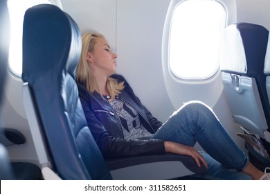 Tired Blonde Casual Caucasian Lady Napping On Uncomfortable Seat While Traveling By Airplane. Commercial Transportation By Planes.