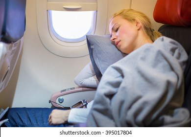 Tired Blonde Casual Caucasian Lady Napping On Uncomfortable Seat While Traveling By Airplane. Commercial Transportation By Planes.