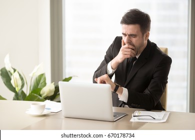 Tired bored businessman yawning at workplace near laptop, looking at wristwatch, checking time, boring work, dead end job, overwork extra after hours, lack of sleep, insomnia consequences, need rest  - Powered by Shutterstock