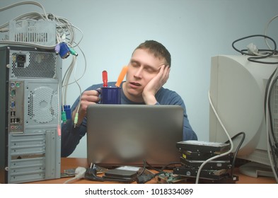 Tired And Bored Computer Repairman Is Sitting On His Workplace And Is Sleeping. Computer Technician Tired From His Work And Users.