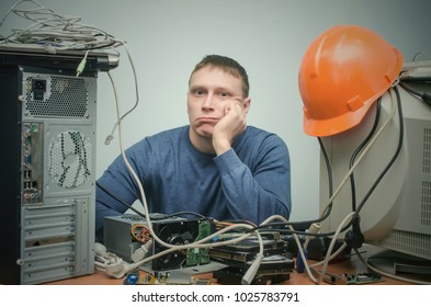 Tired And Bored Computer Repairman Is Sitting On His Workplace And Thinking. Computer Technician Tired From His Work And Users.