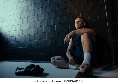 Tired boxer resting in dark gym after exercising near boxing gloves on the floor. - Powered by Shutterstock