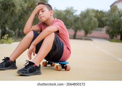 Tired Boy Sitting On Skateboard.