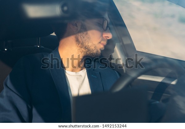 Tired business man falling\
asleep sitting inside her car seen through windshield, stopped to\
rest after driving. Exhausted, sleepiness, overworked driver\
concept.