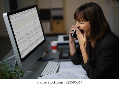 Tired Businessman At Her Desk, Showing Yawning Gesture While Talking To Someone On Mobile Phone.