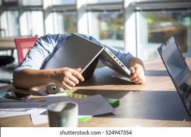 Tired businessman sleeping after hard working day in office interior. Man lying on table with laptop computer on. Business concept.