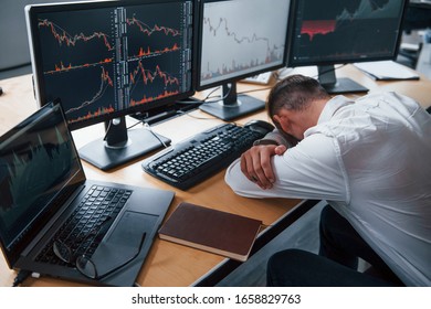 Tired businessman sleeping on the workplace by leaning on the table with multiple screens on it. Stock information on displays. - Shutterstock ID 1658829763
