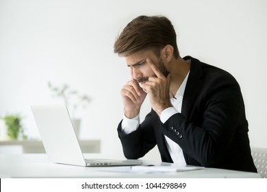 Tired businessman squinting eyes looking at laptop screen trying to focus concentrate, office employee thinking of online problem suffering from fatigue, headache or bad sight, computer syndrome